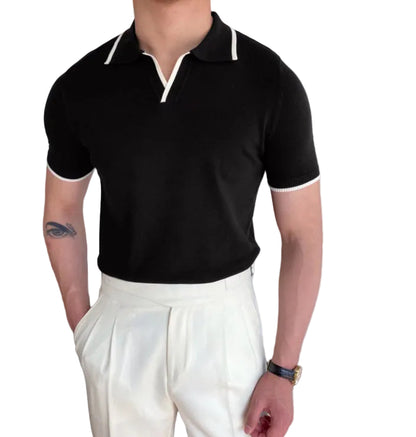 Person wearing a black polo shirt with white trim and white pants indoors.
