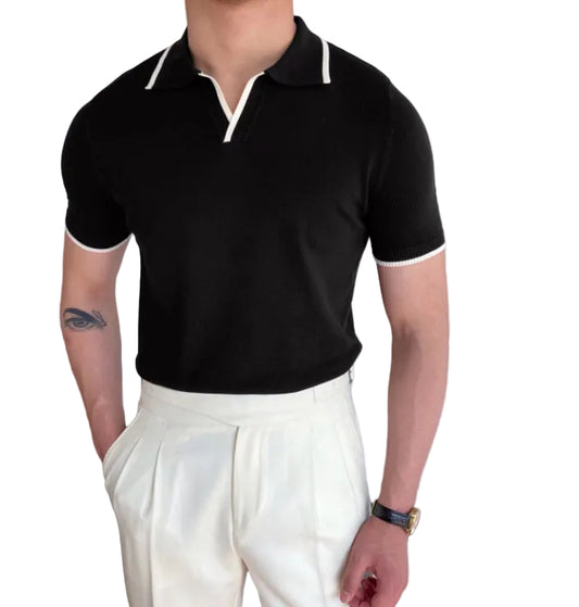 Person wearing a black polo shirt with white trim and white pants indoors.