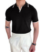 Person wearing a black polo shirt with white trim and white pants indoors.
